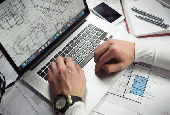 Architect reviewing detailed floor plans and schematics on a laptop with a smartphone nearby.