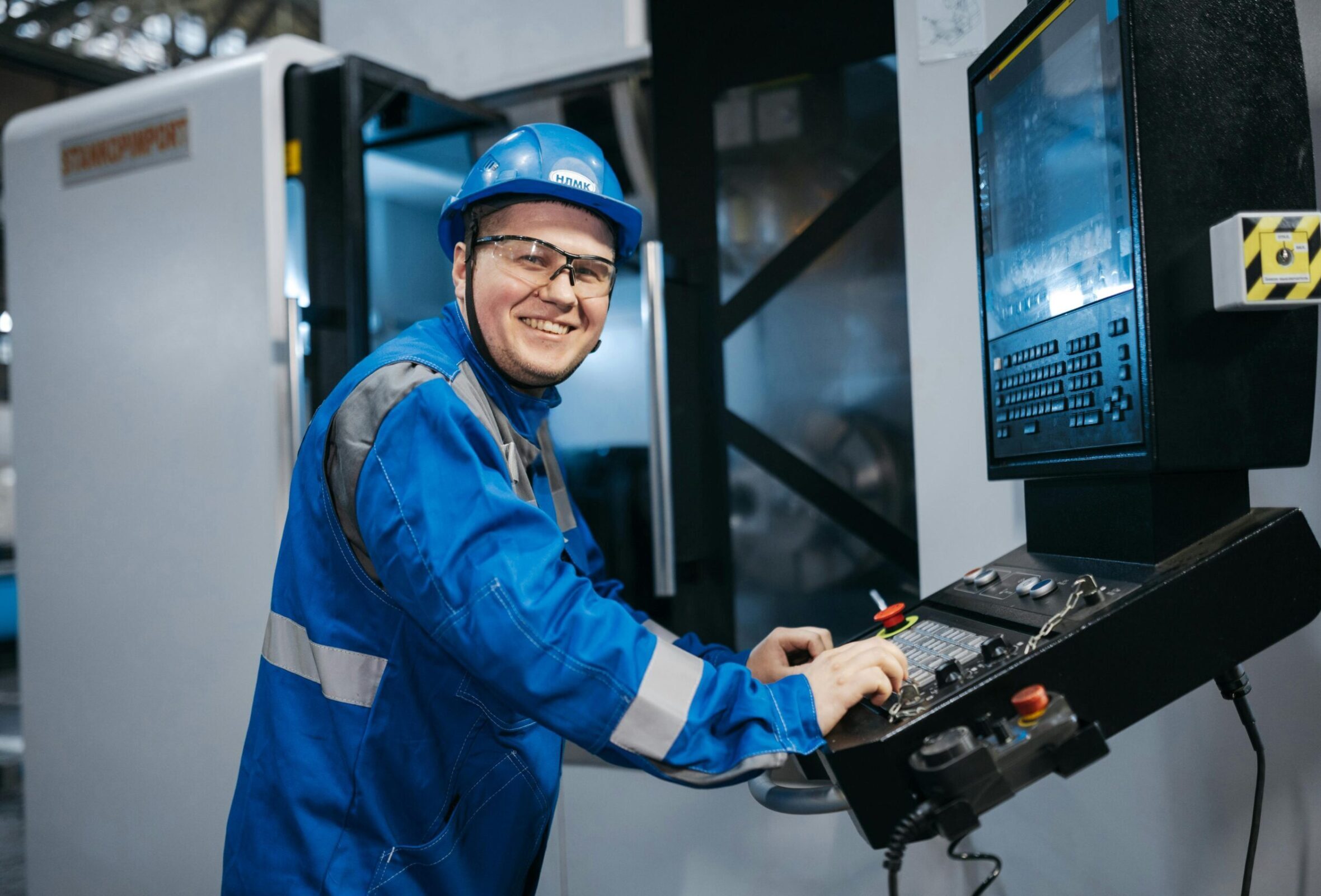 Smiling worker in blue uniform and hard hat using CNC machine indoors in Russia.