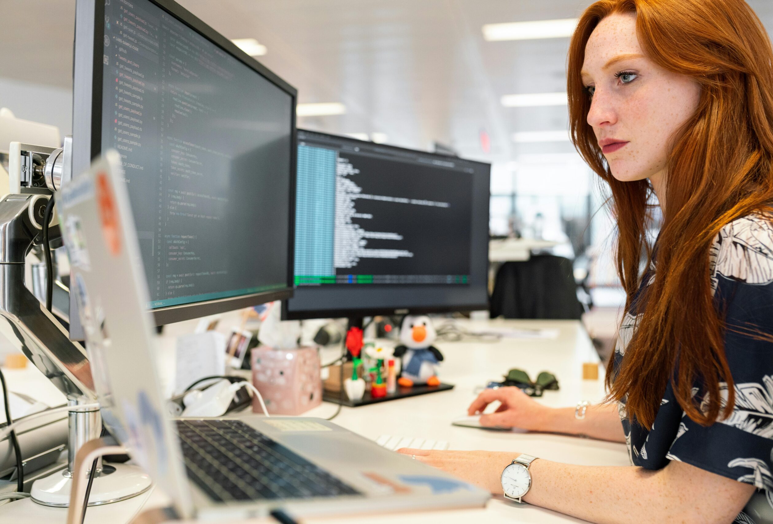A focused female software engineer coding on dual monitors in a modern office.